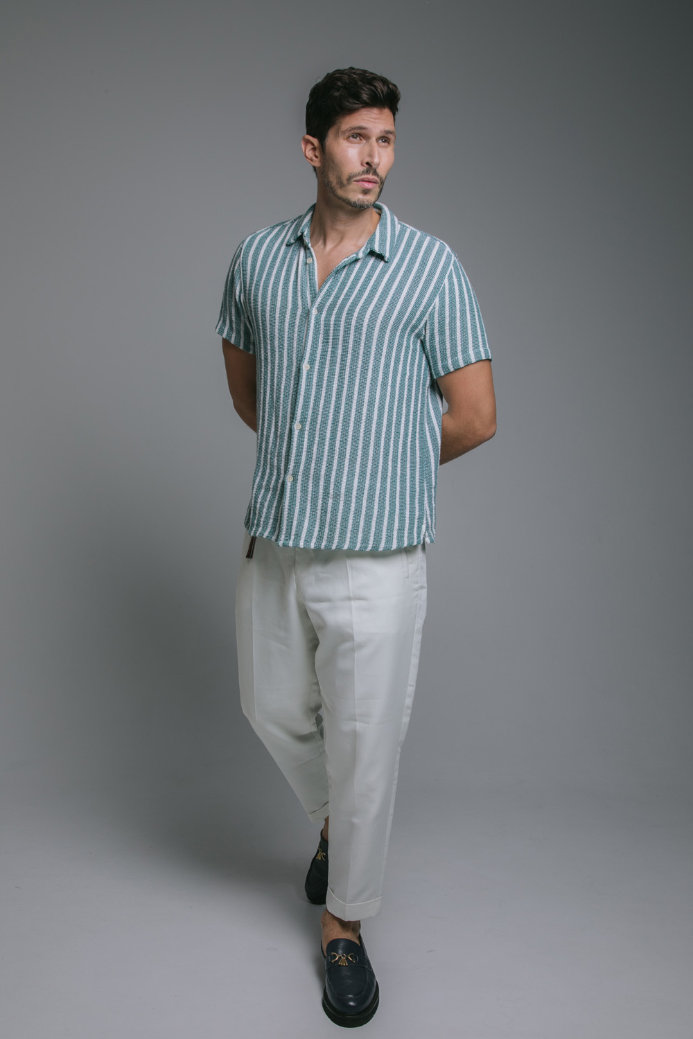 Full body image of Alexander Devrient in a striped shirt and white trousers.