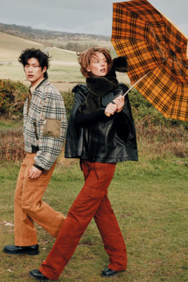 Two models walking with an orange checkered umbrella from Burberry umbrella autumn winter 2025 dragged back by the wind