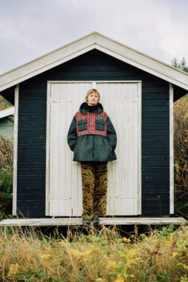 Woman in tartan wax jacket stood in front of boat shed