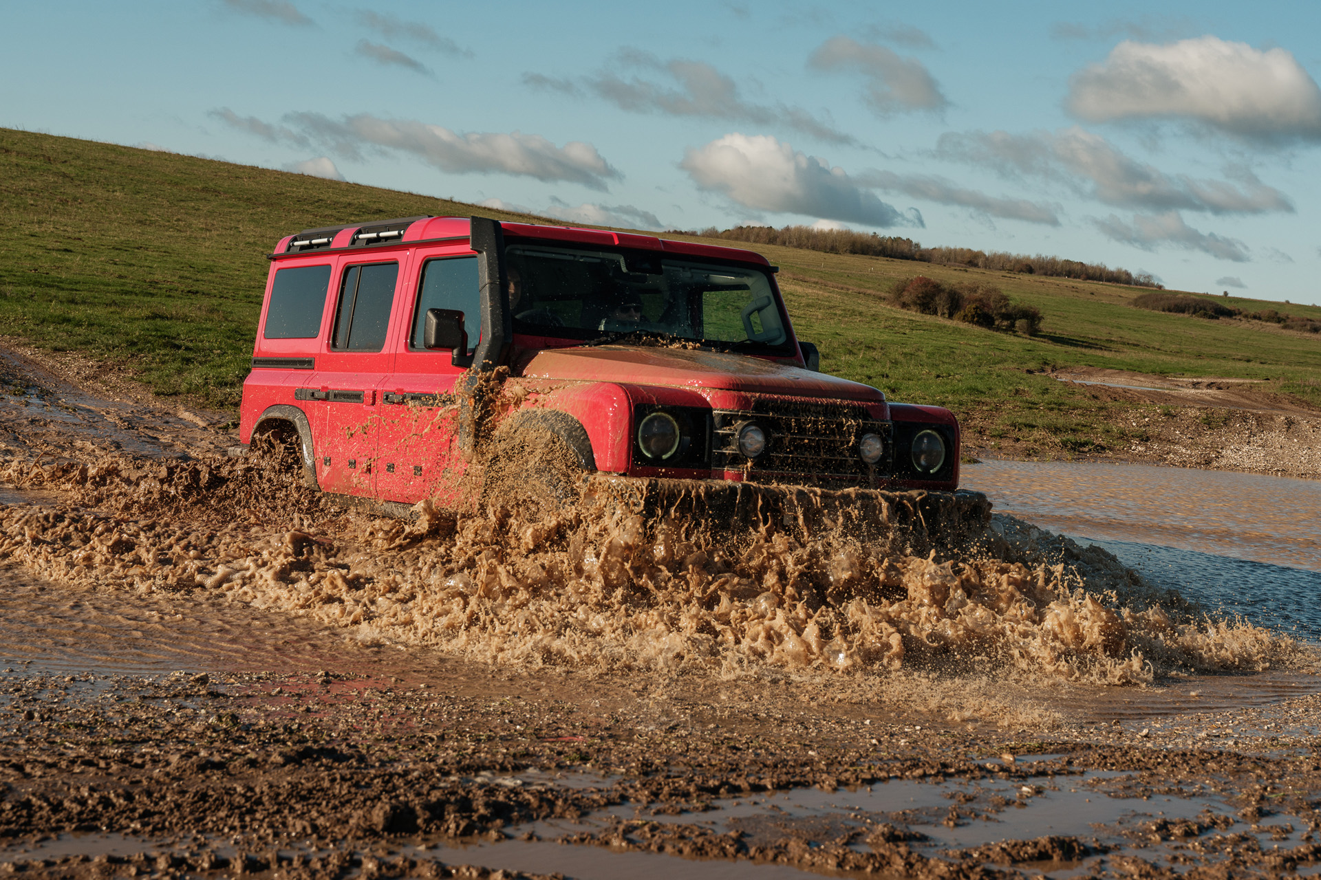 Red Ineos Grenadier driving through mud