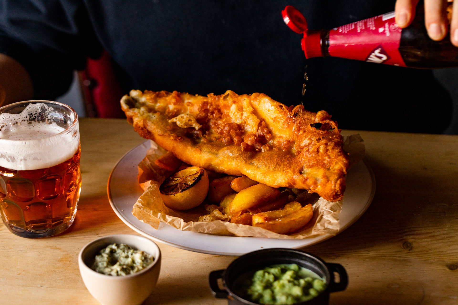 Someone pours vinegar onto fish and chips