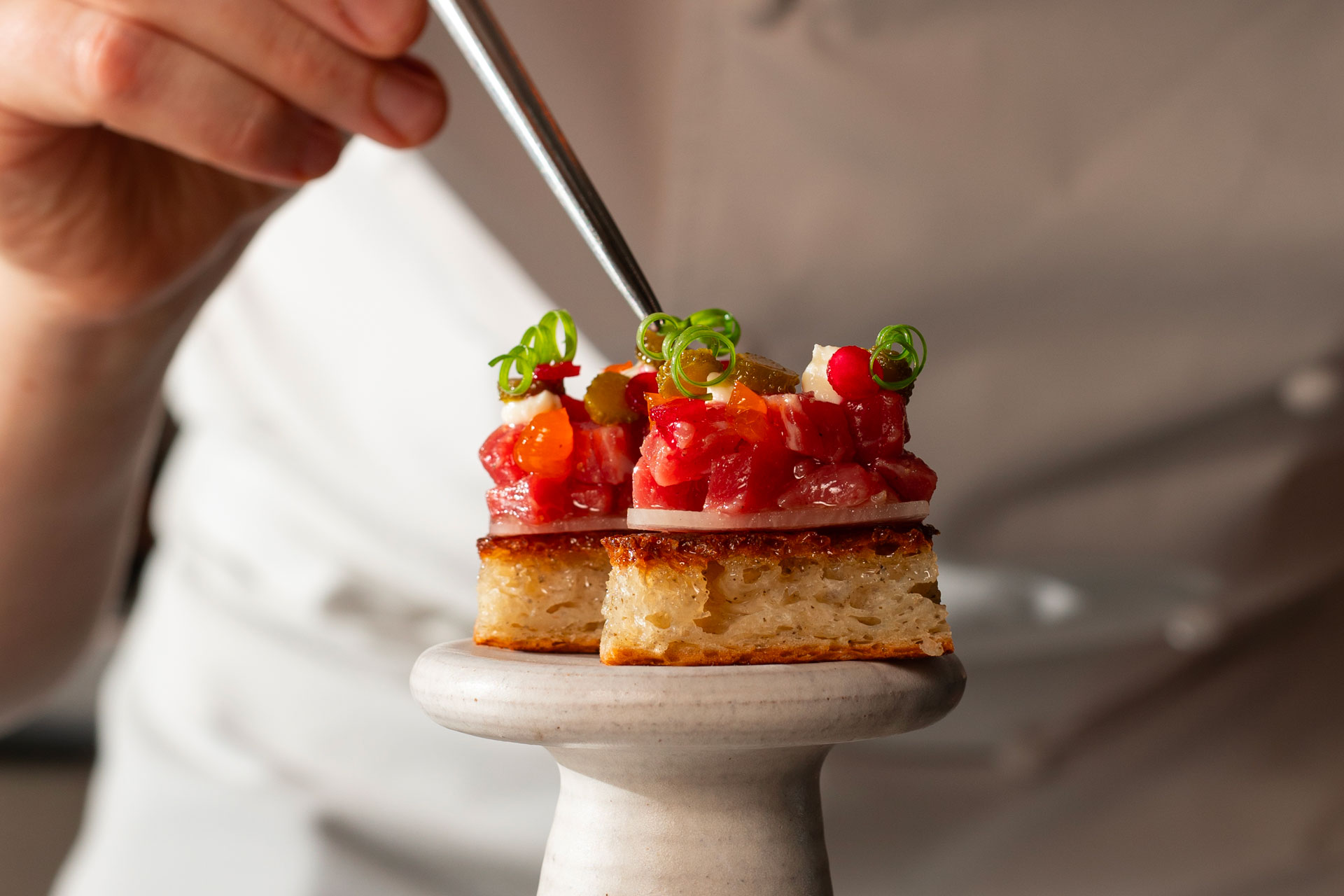 Someone tweezing a green ingredient onto a tartare dish