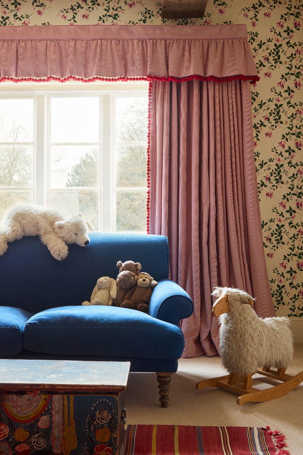 Girls' room with red and pink curtains and wallpaper, and blue armchair decorated with stuffed toys
