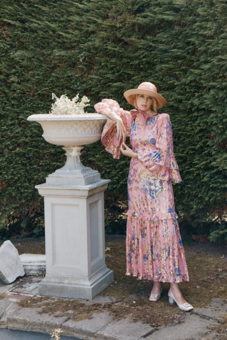 Woman leaning on stone case in garden, wearing vintage-inspired outfit from Queens of Archive | female founded british fashion brands