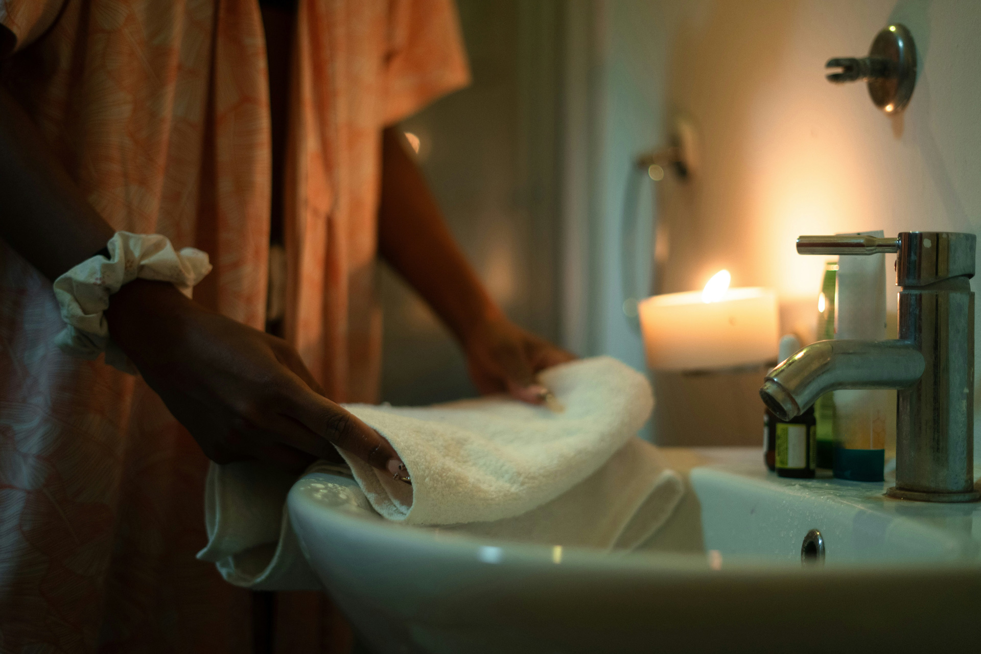 A woman folding a towel in a candlelit bathroom