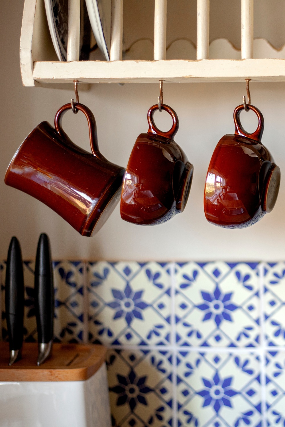 Burgundy mugs hung above blue tiled wall