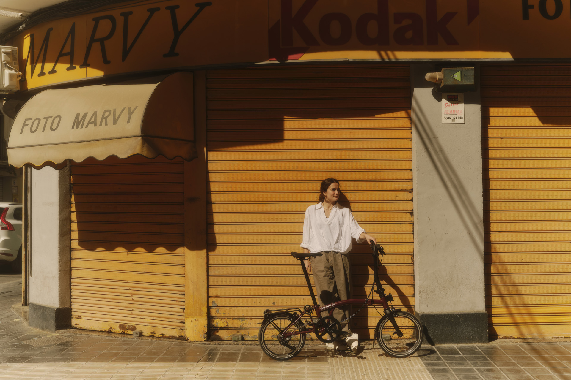 A woman standing with a Brompton against a yellow shuttered shop