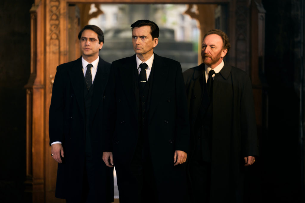 Three men dressed in black for a funeral.