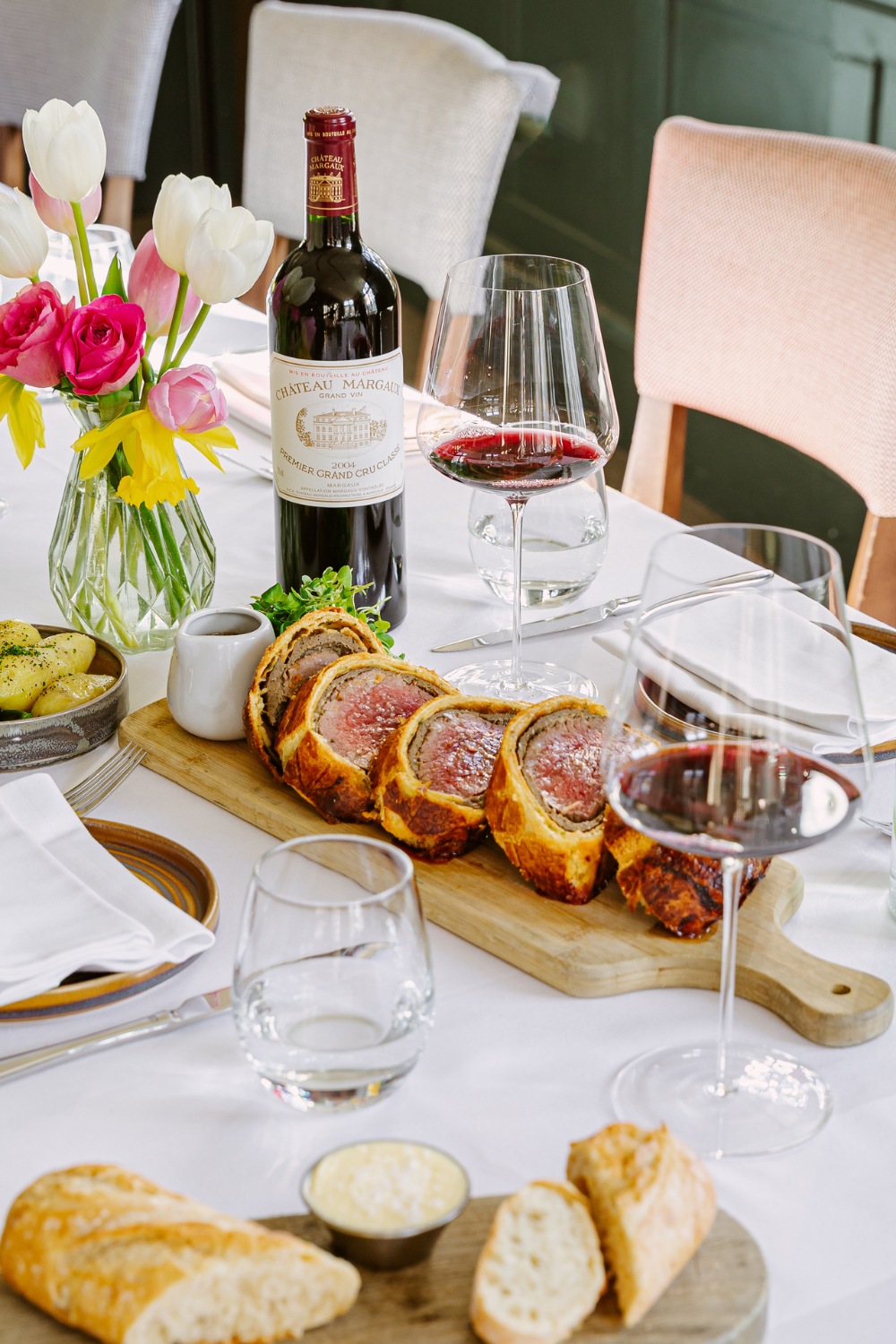 Beef wellington set on table with glasses of wine and vase of flowers