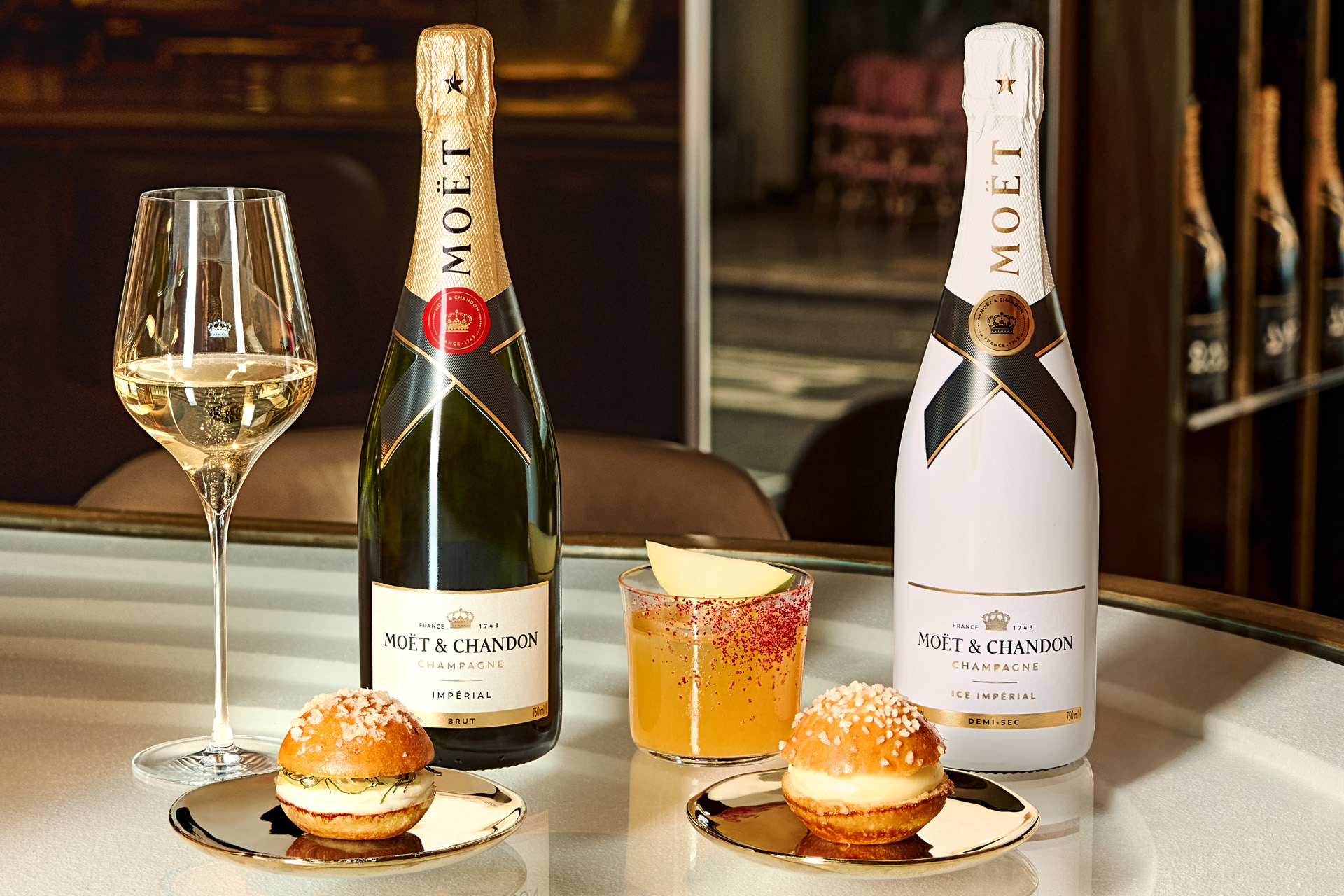 Two bottles of Moët & Chandon beside two glasses and two snacks