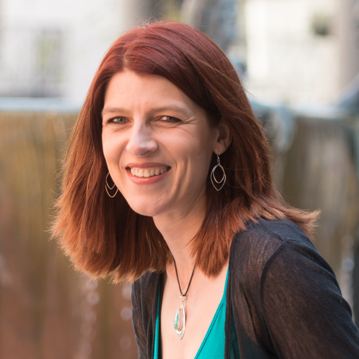 A headshot of Nicky Goulder, a white woman with mid length auburn hair, smiling and looking at the camera