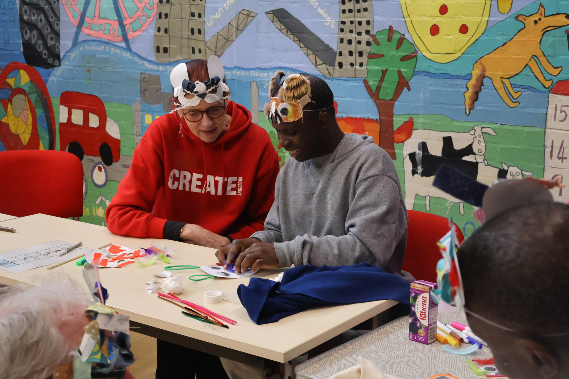 A woman wearing an animal face mask helping a man to create another one