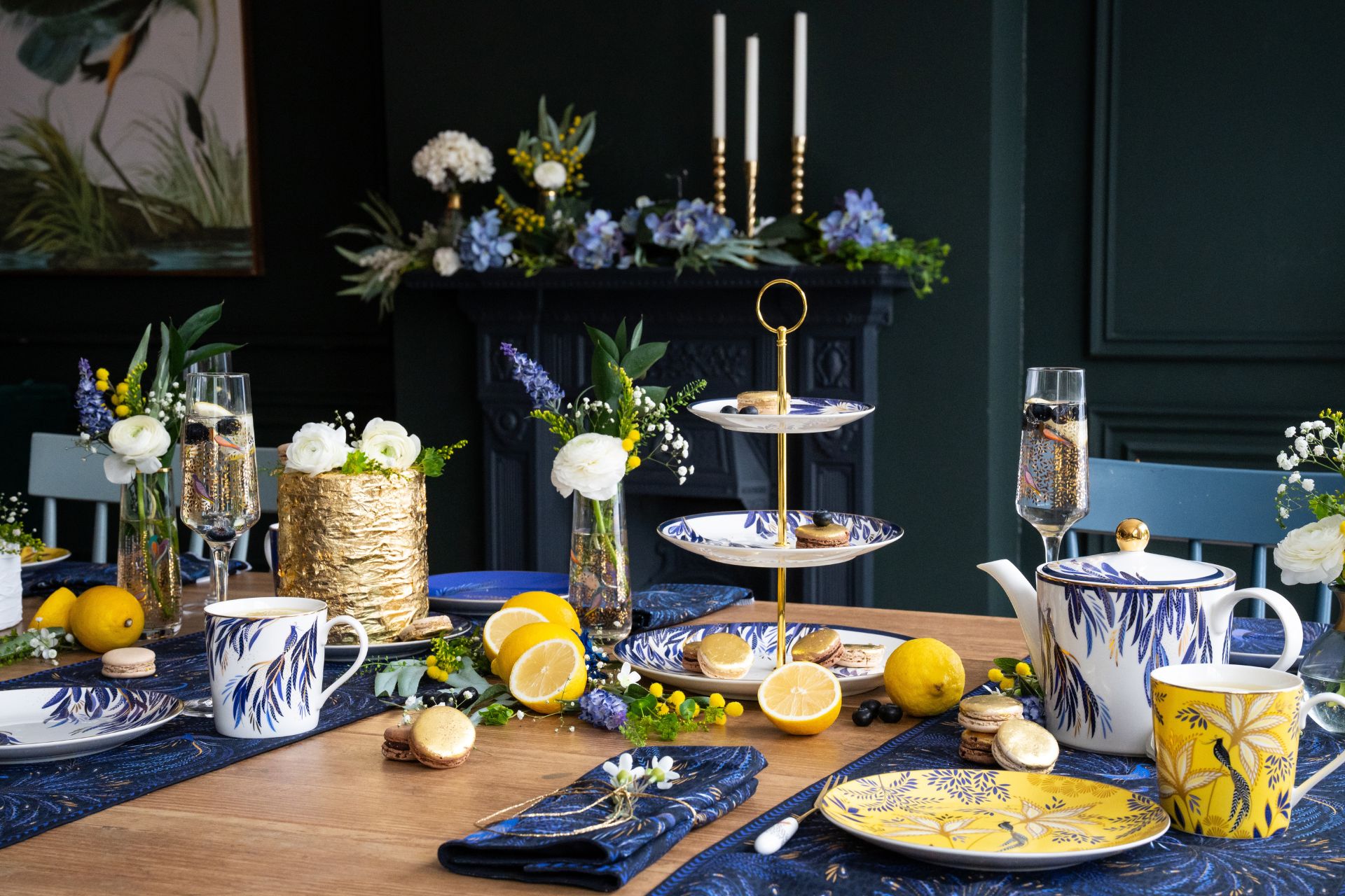 Wooden table set with blue, yellow and white plates, place mats and glasses, as well as lemons and cakes