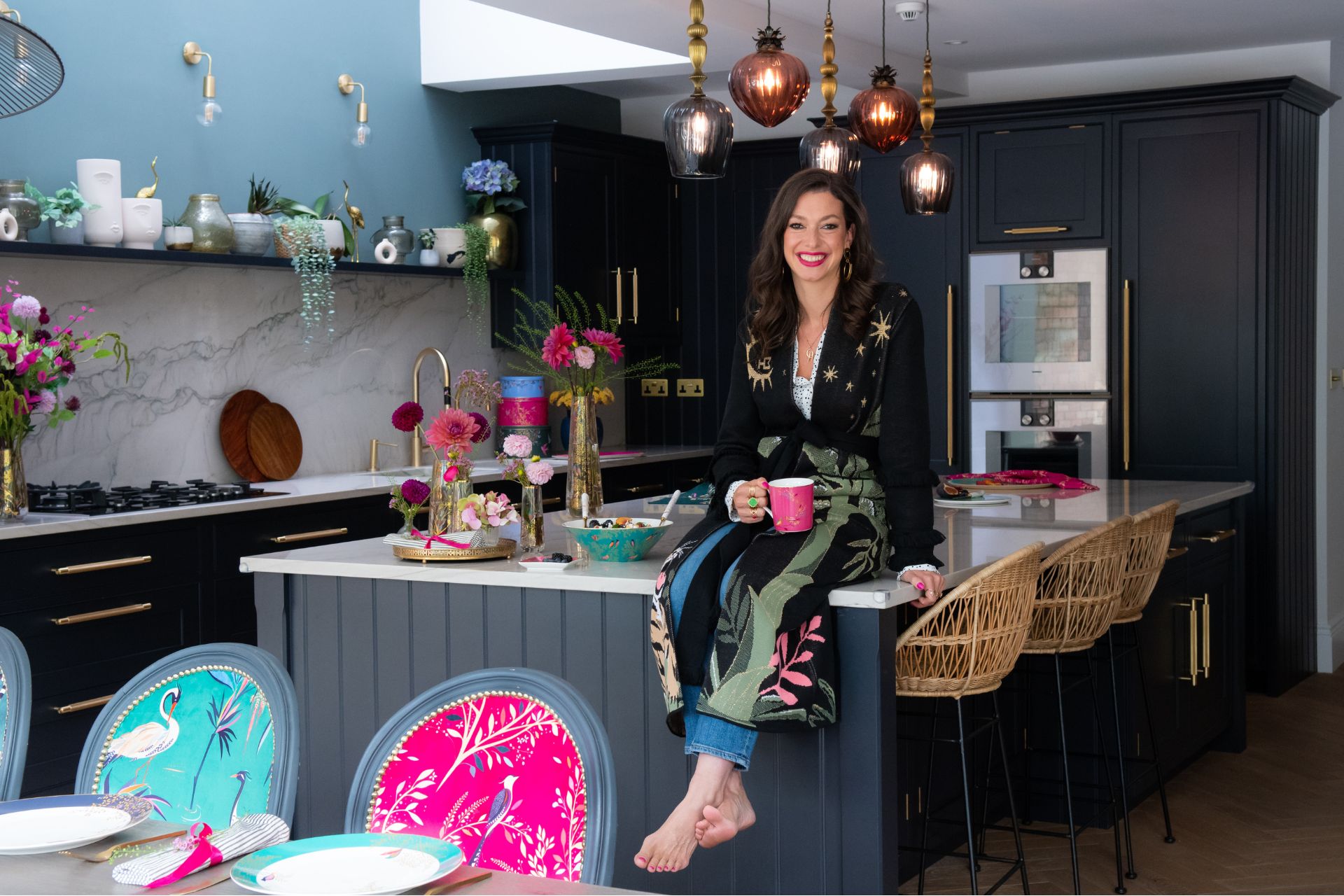 Sara Miller sat on kitchen island in robe, holding mug