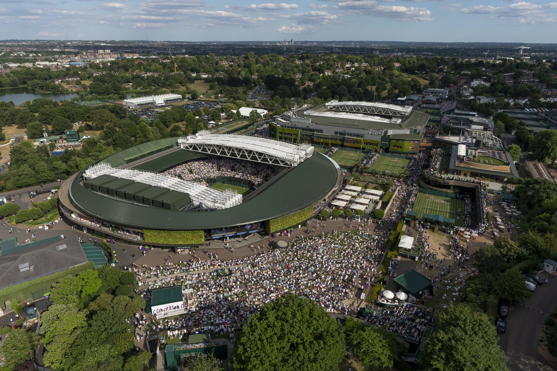Aerial view from behind The Hill towards a packed No.1 Court and Centre Court in the distance at The Championships 2025