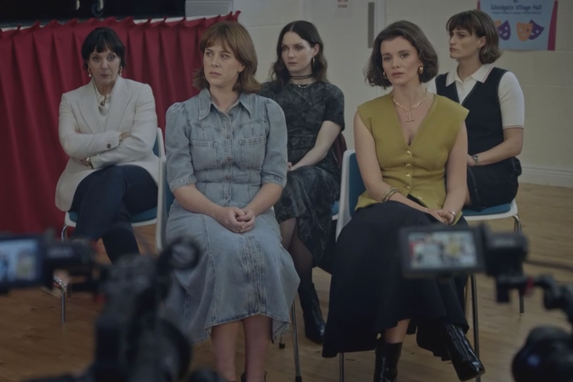 A group of women dressed in nice clothes sit opposite a television camera.