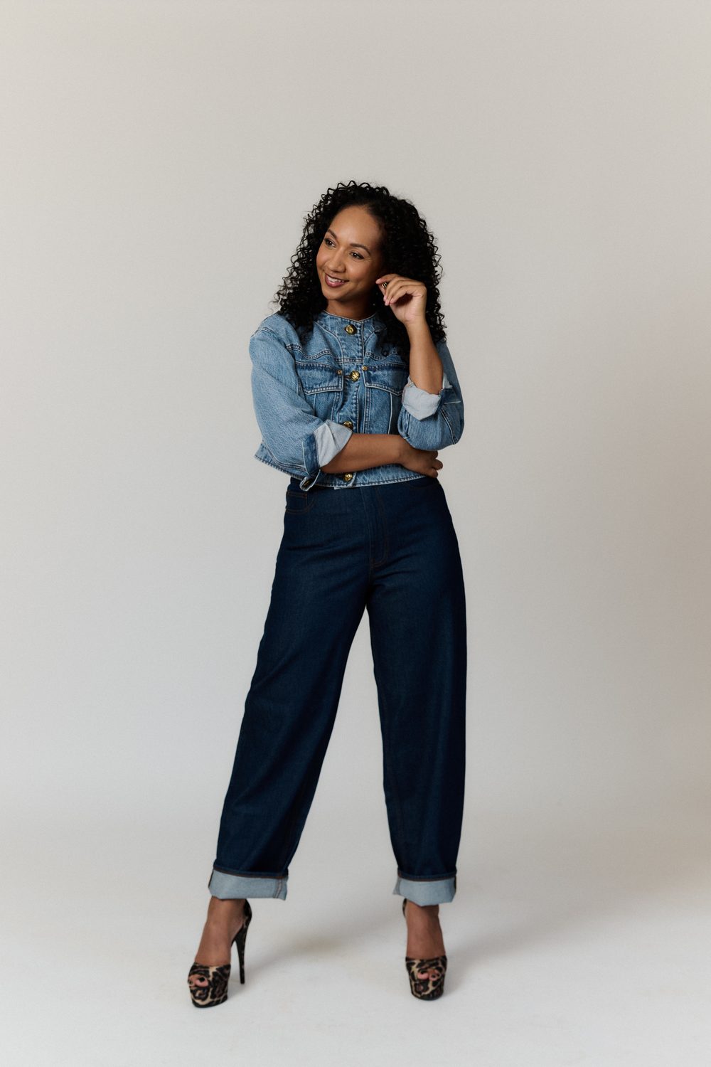 Alexandria Riley wearing a denim jacket and darker denim jewels, crossing her arms and smiling off camera