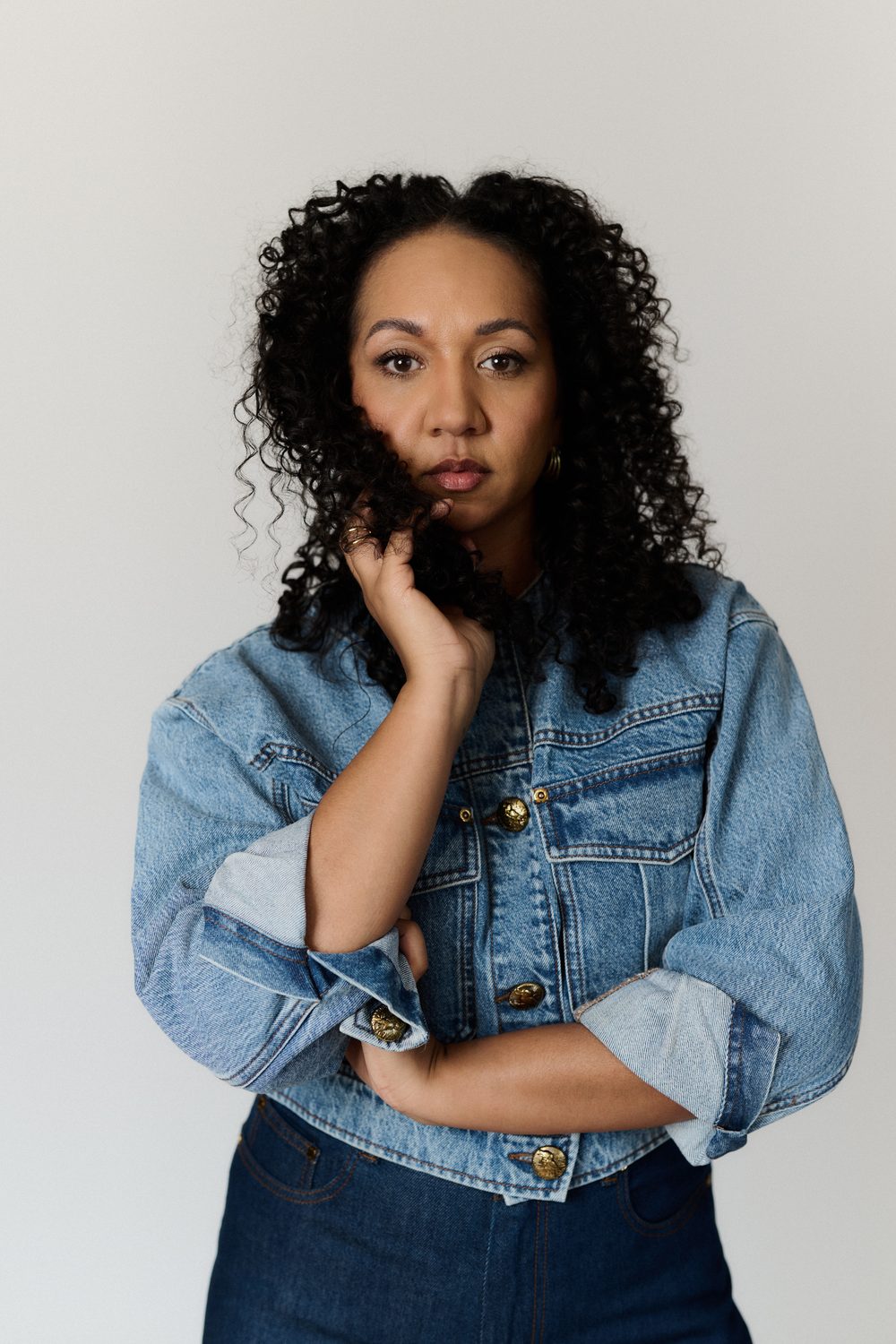 A closer-up shot of Alexandria wearing a denim jacket, touching her hair close to her face.