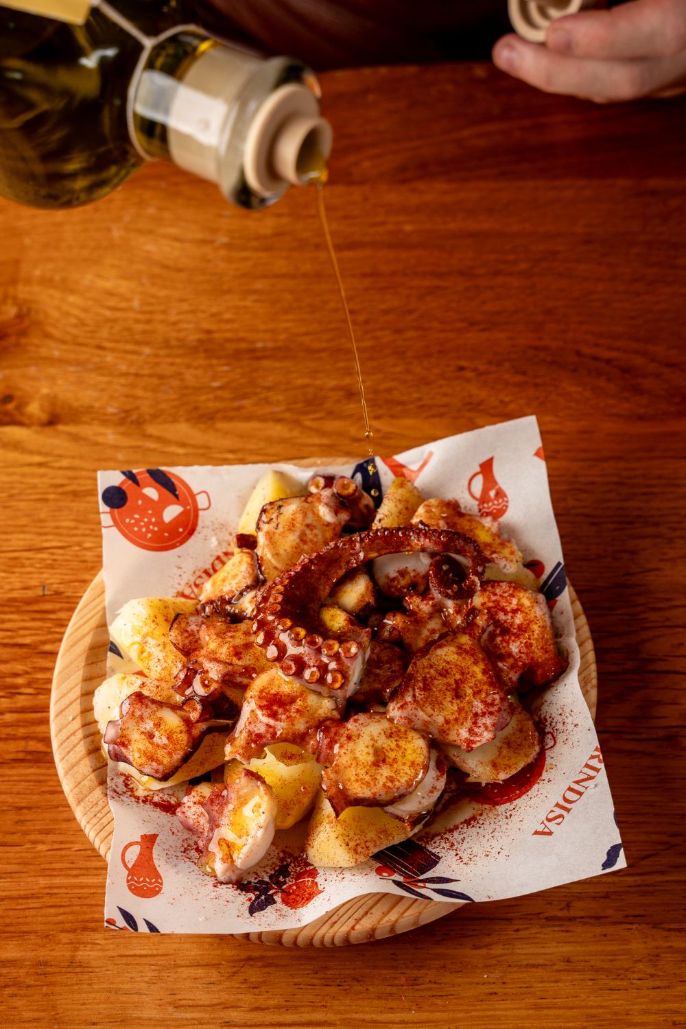 Olive oil being poured over octopus and potatoes