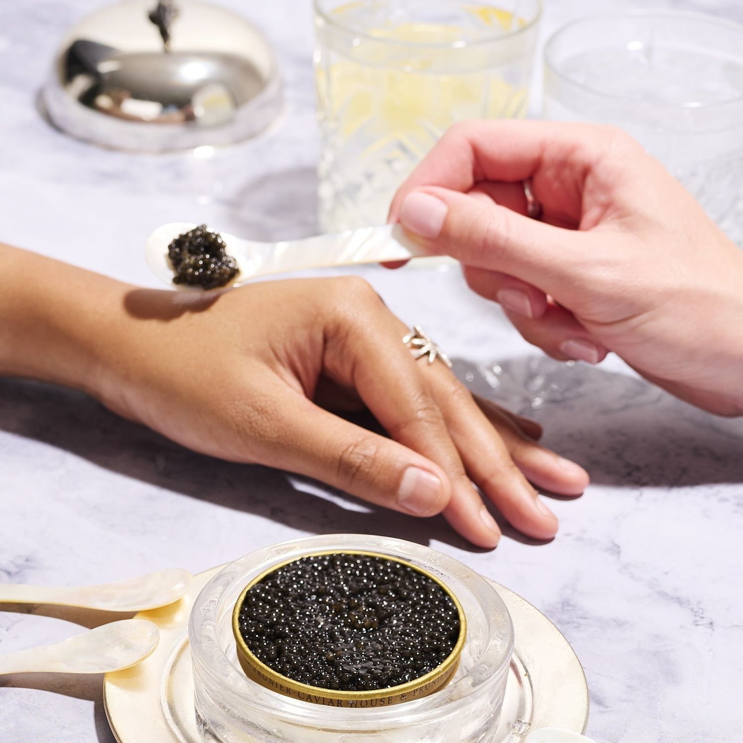 An image of two hands resting on a table. One is laying a spoon of caviar onto the other.