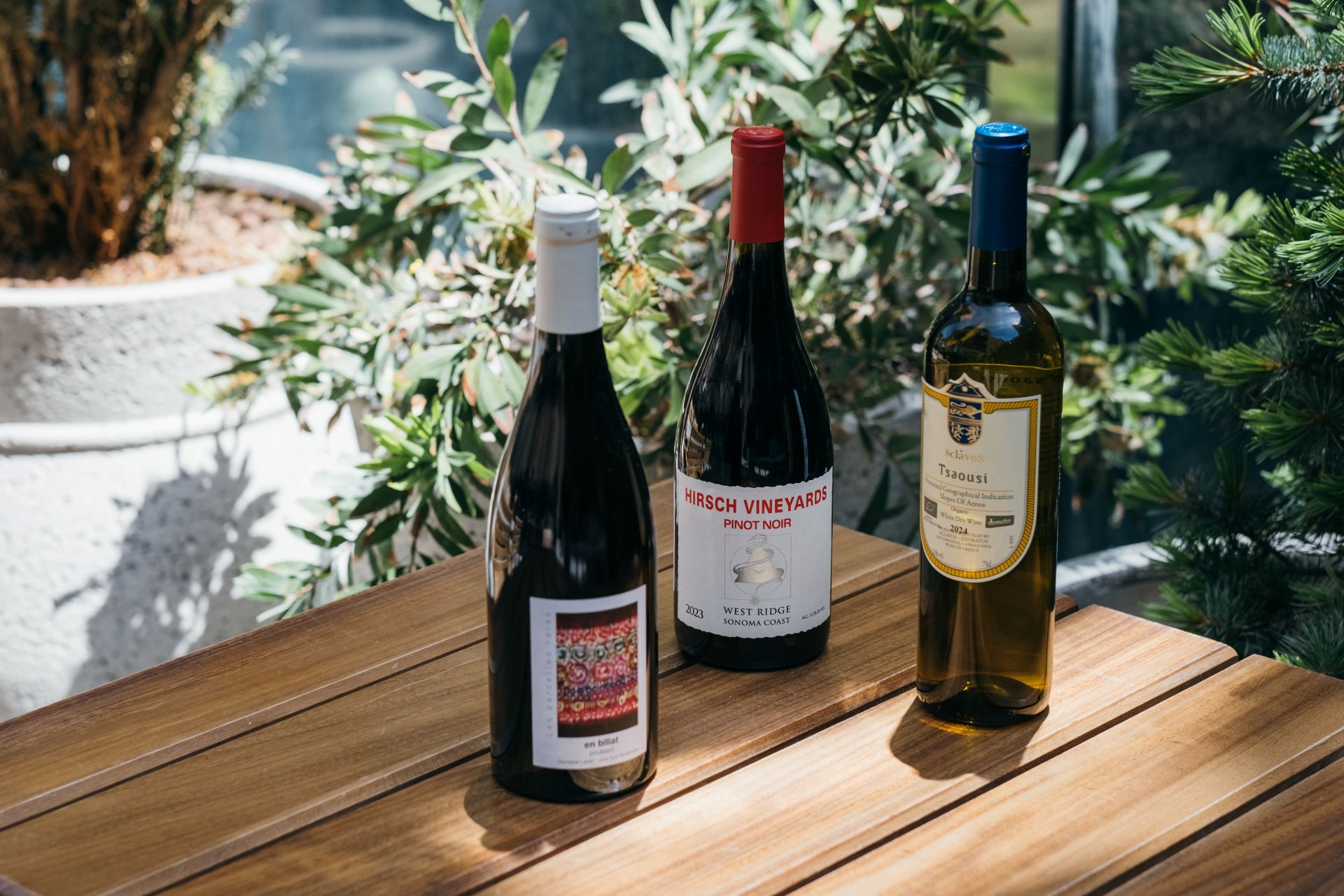 Three bottles of wine on a table outside beside plants