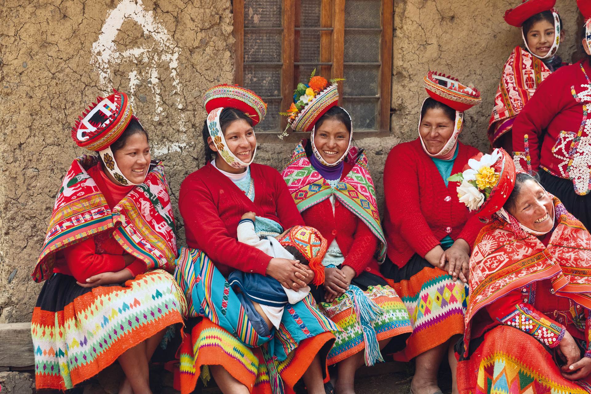Women from the Huilloc Community in Peru, dressed in traditional clothing, sat as a group, smiling and laughing.