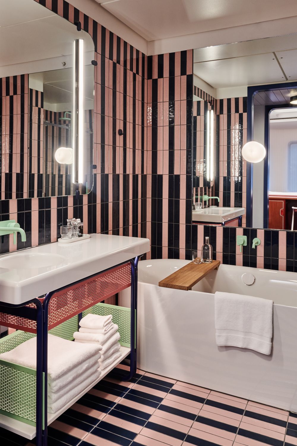 A stylish bathroom with pink striped tile walls, a sink and a large bathtub
