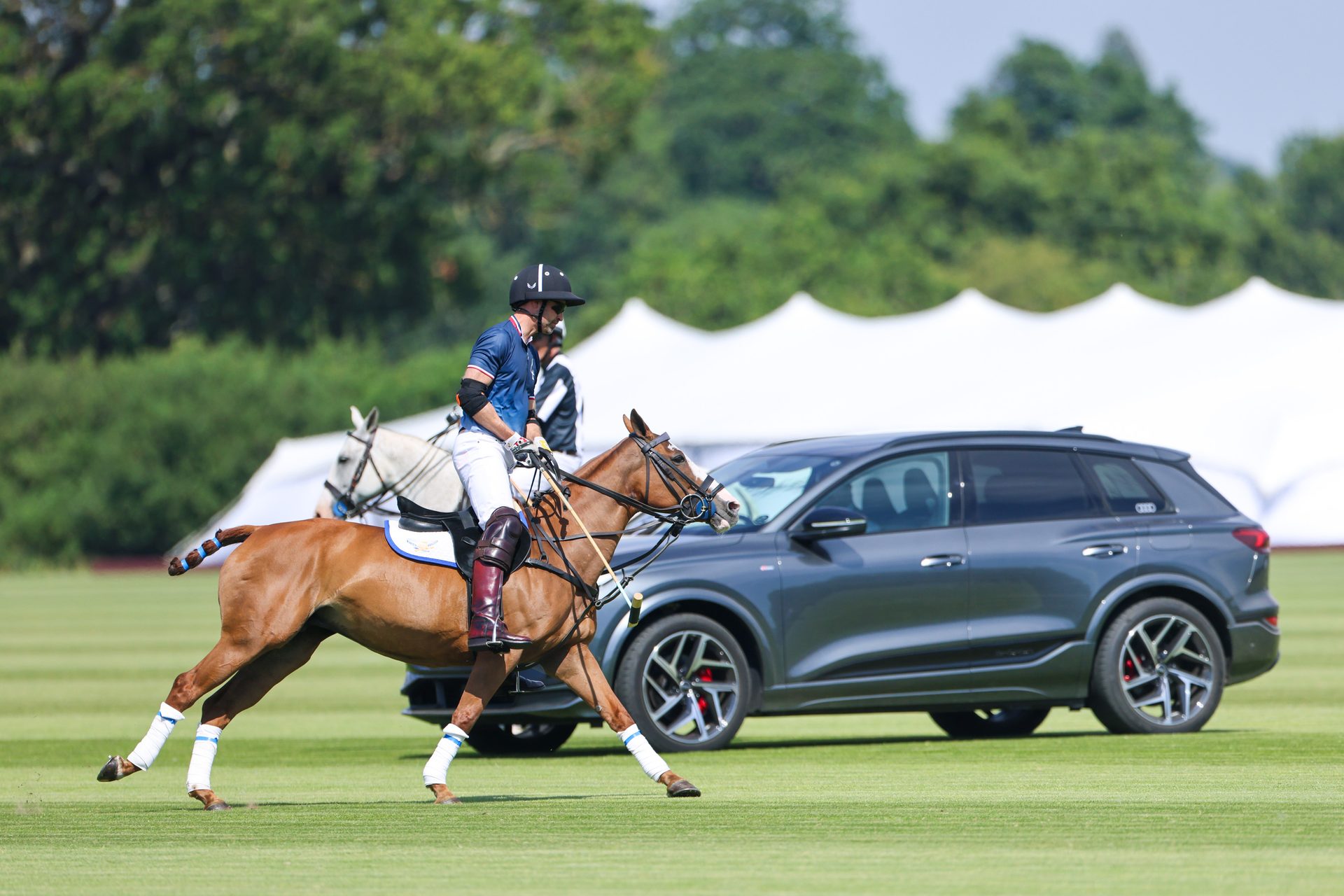 Prince William in a polo uniform, galloping on a horse in front of the Audi Q6 car