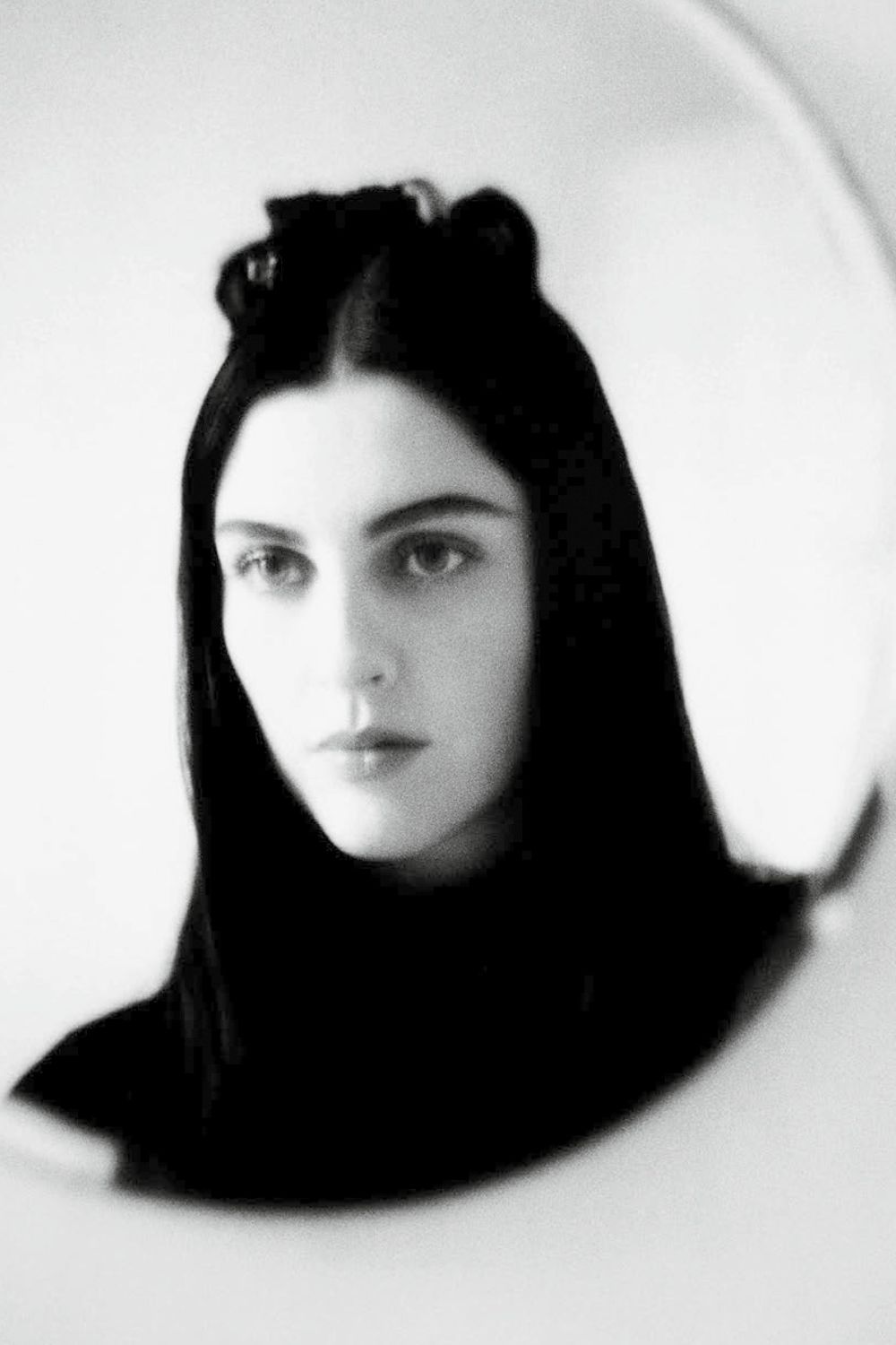 A black and white image of Susie Cave looking into a round mirror