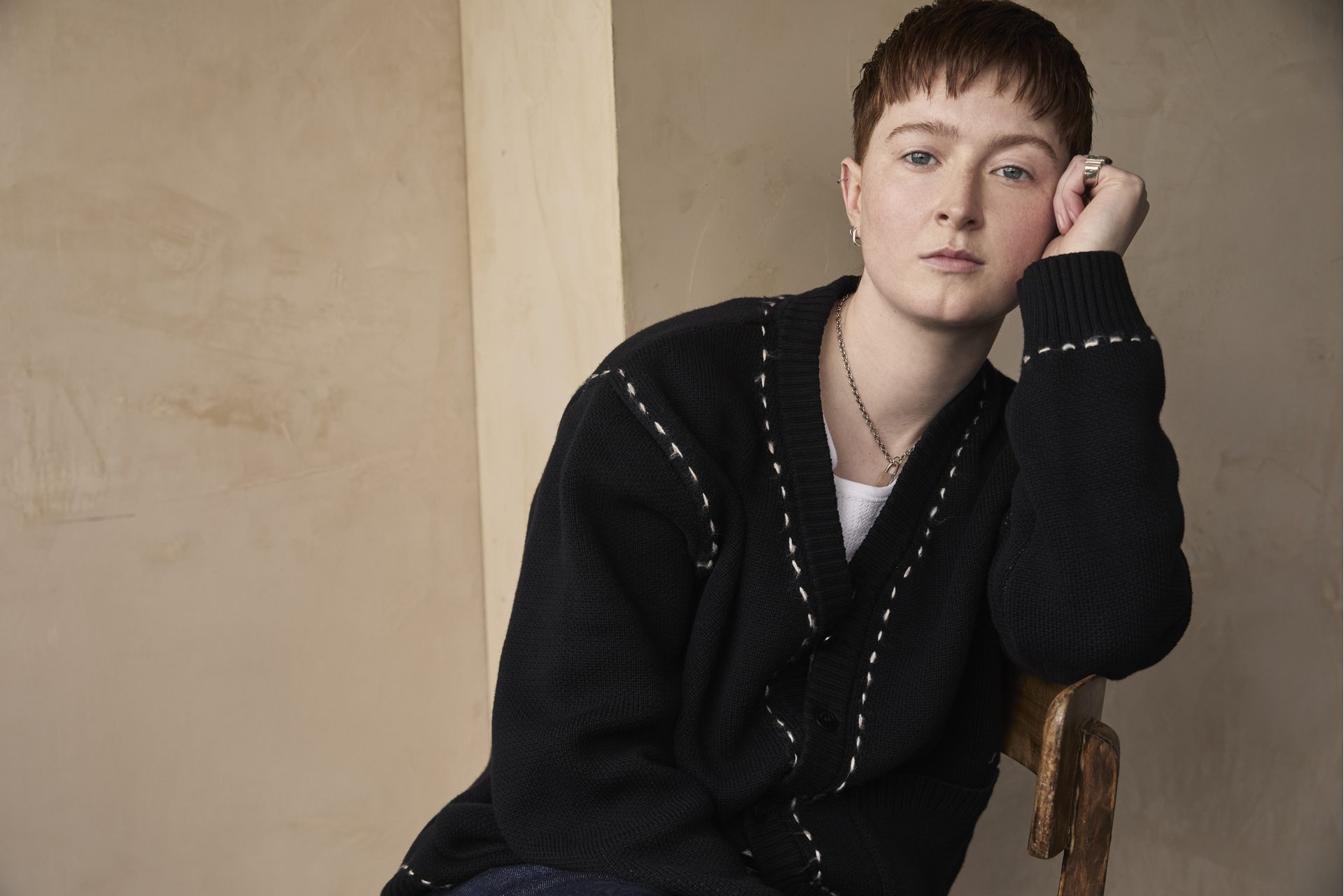 Rex from the waist up, leaning sideways on a chair, resting their head in their hand