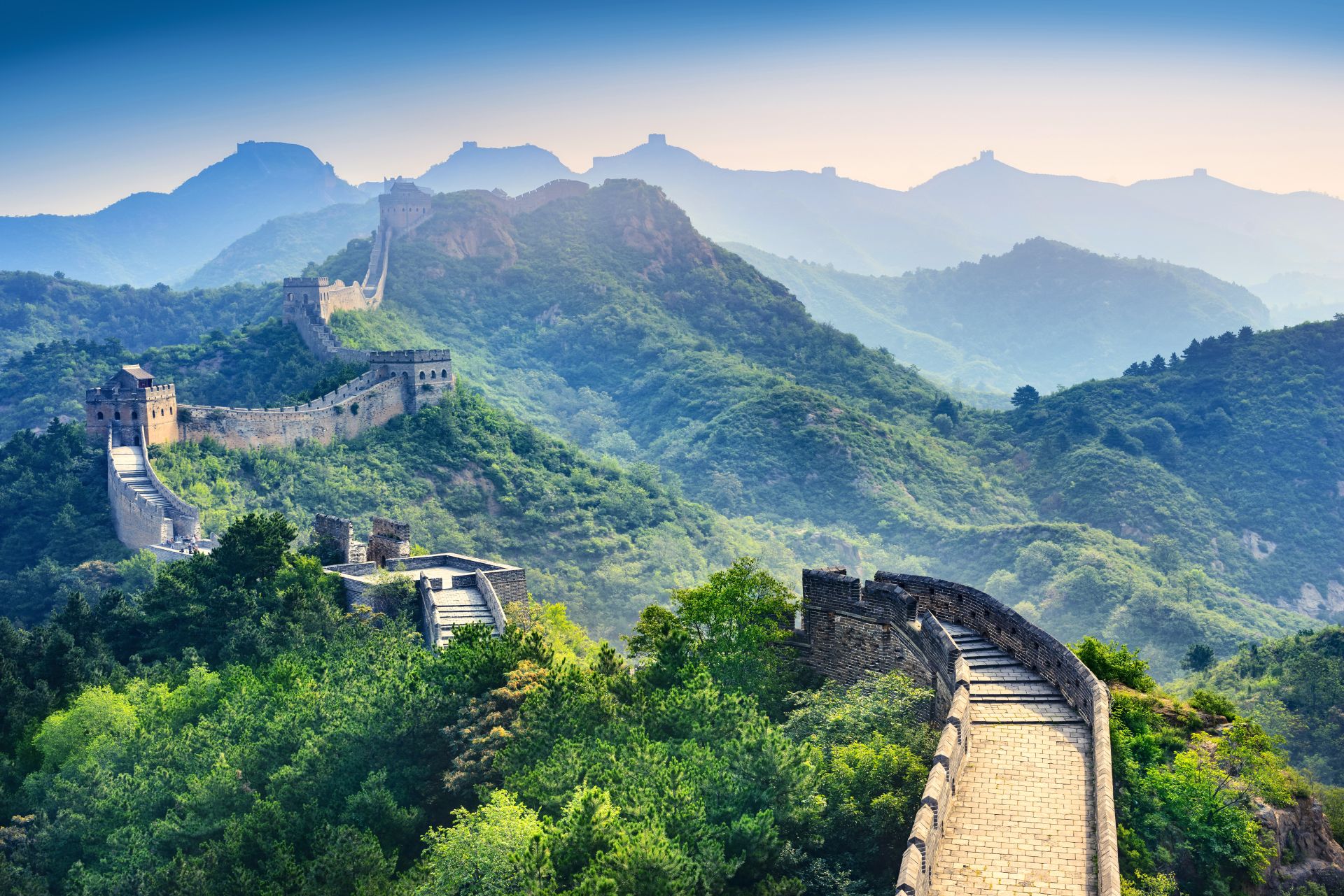 The Great Wall of China cutting through green treed hills, with a light mist