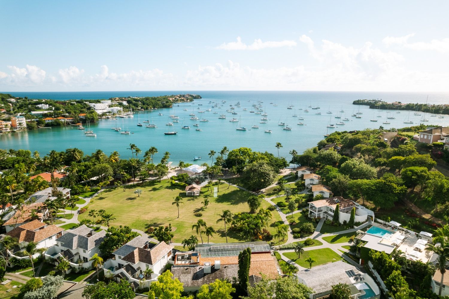 Wide overhead shot of a lush green resort in Grenada sat right on the coast of a boat-filled cove