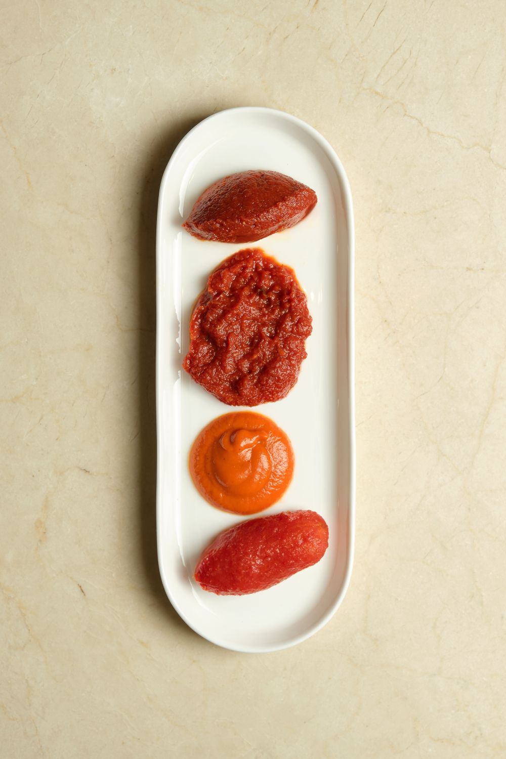 Four red blobs of tomato on a white plate.