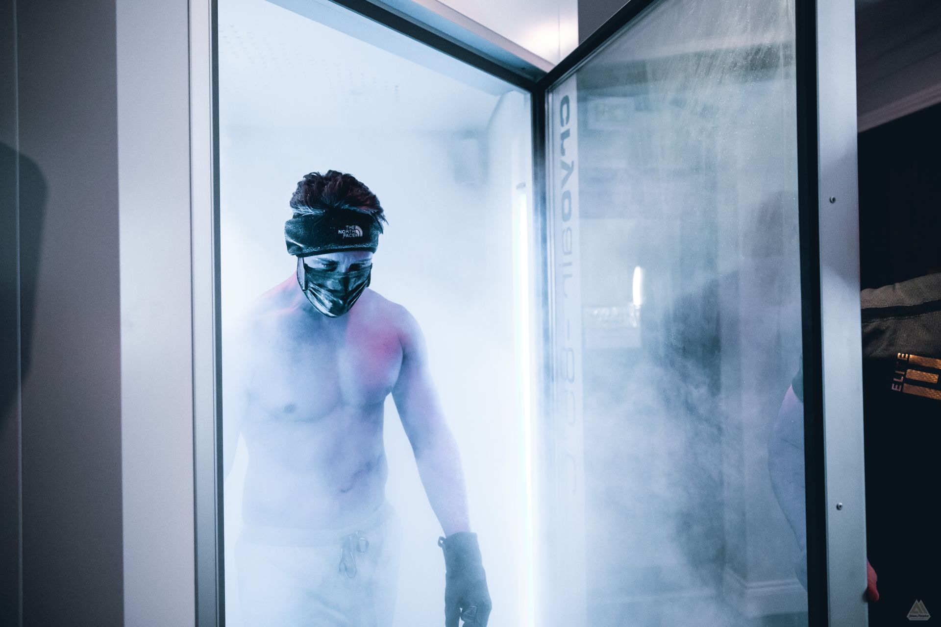 A shirtless man emerging in a cloud of mist from a cryotherapy chamber