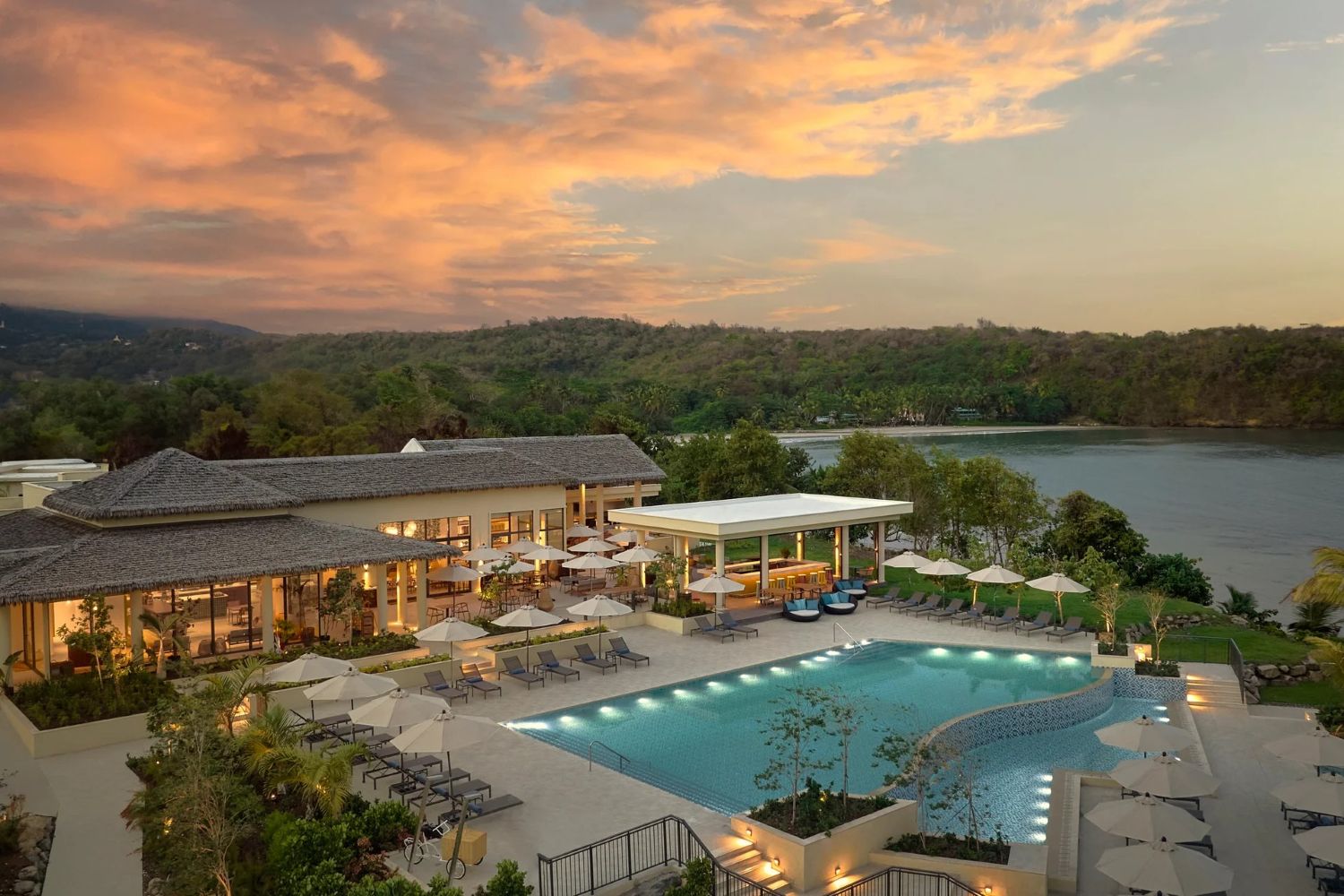 A seaside resort at dusk with a large pool and low rise buildings