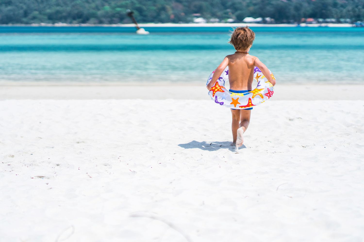 A young child running across white sand into a bright blue sea