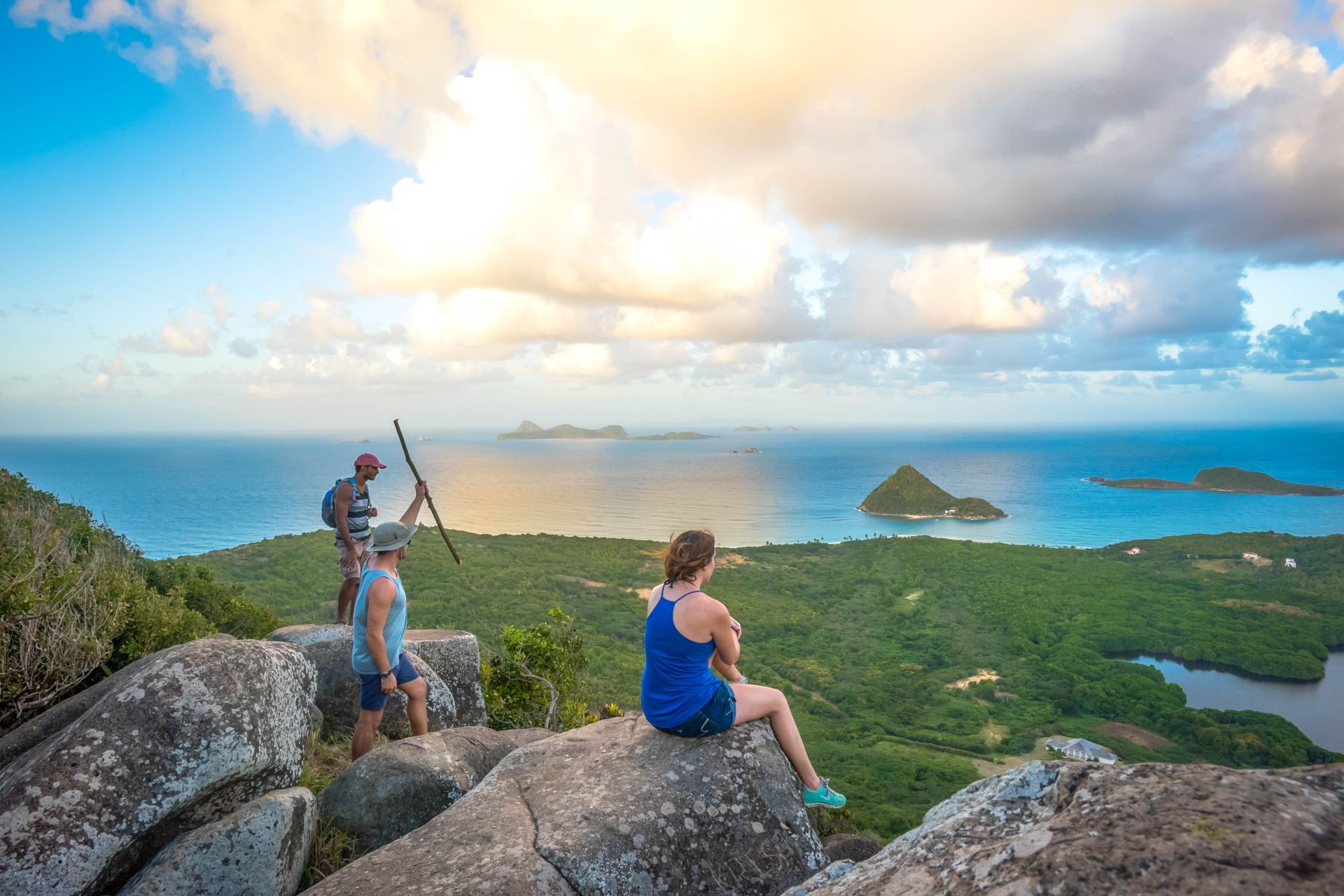 Hikers sitting on rocks at the top of a cliff overlooking a tree-covered island and the sea at dawn