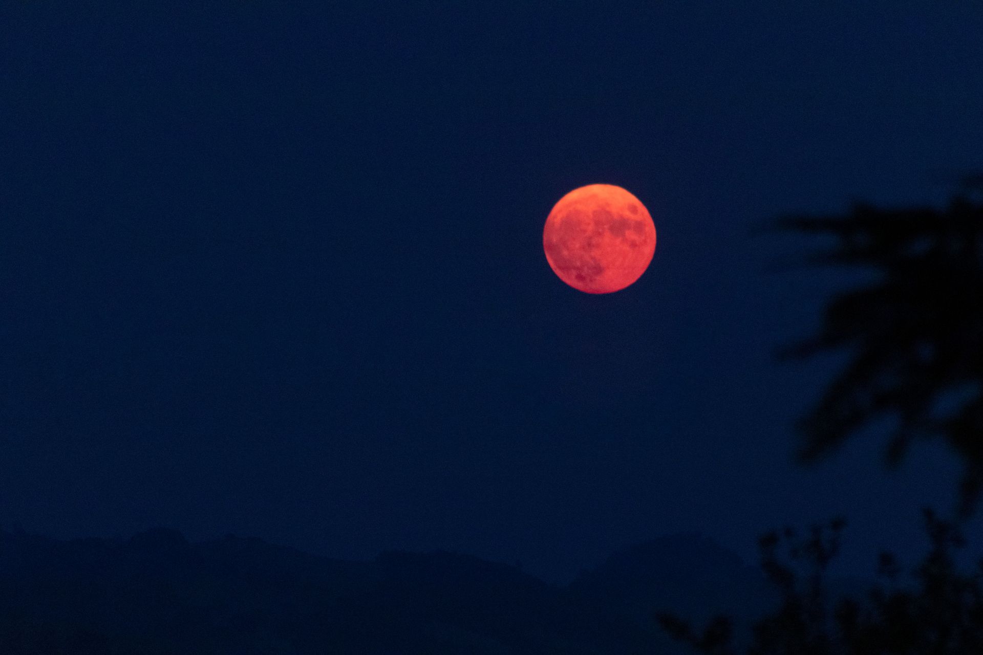 A captivating blood moon rising over a tranquil, silhouetted landscape at night